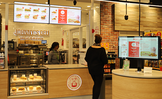 The order counter at 7-Eleven with Johnny's Deli, customer is collecting her order.